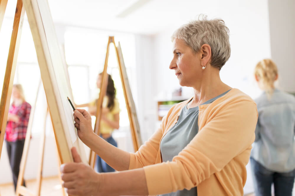 Older woman drawing on easel in class