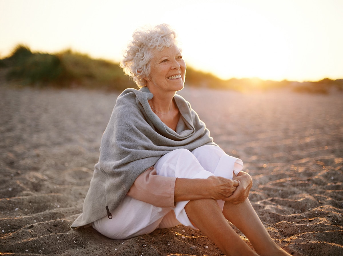 Happy woman sitting on a beach at sunset